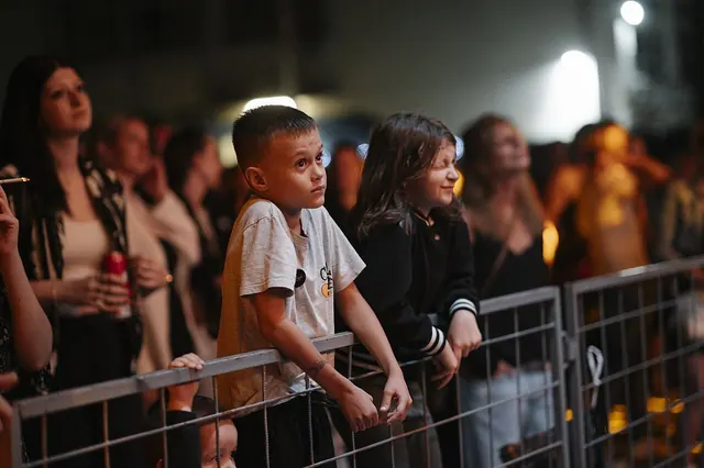 Children watch intently at a lively outdoor music festival on a warm summer evening